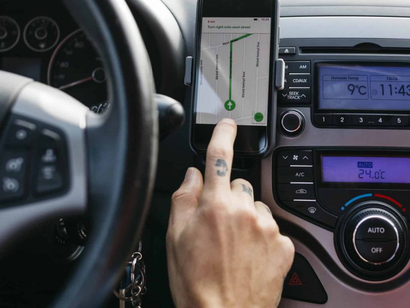 Close-up of man with tattooed hand driving car using cell phone as navigation system